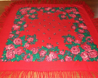 May include: A red square scarf with a floral pattern of pink roses and green leaves. The scarf has a fringe border.