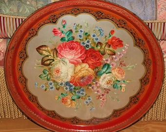 May include: A red and gold painted metal tray with a floral design. The tray features a bouquet of red, pink, white, and blue flowers with green leaves. The tray has a scalloped edge and a black and gold border.