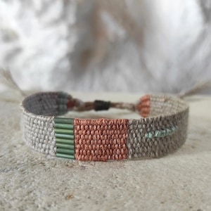 Può includere: Braccialetto intrecciato nei toni del grigio, corallo e verde. Il braccialetto presenta una sezione centrale color corallo affiancata da fasce grigie intrecciate. Perline verdi aggiungono colore. Chiusura regolabile.