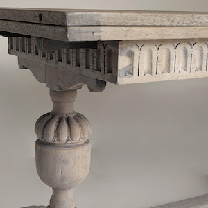 May include: A light-coloured wooden table with a detailed, carved apron and a pedestal base. The table has a rectangular top with a folding leaf. The base features a bulbous, floral-like design. The table's dimensions are approximately 183 cm long, 91 cm wide, and 76 cm high.