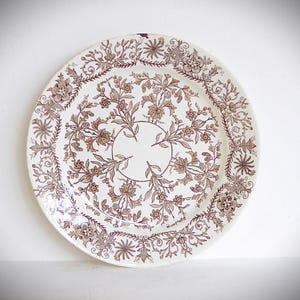 May include: A white ceramic plate with a brown floral pattern. The plate has a raised rim and a delicate design.