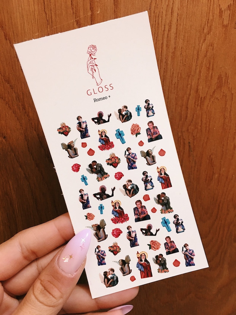 May include: A sheet of nail stickers with a variety of images, including a couple, a cross, a heart, and a rose. The stickers are on a white background and have a glossy finish. The text "GLOSS Romeo+" is printed at the top of the sheet.