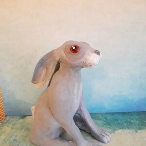 May include: A gray ceramic rabbit figurine with red eyes. The rabbit is sitting with its head tilted up and its ears perked up.