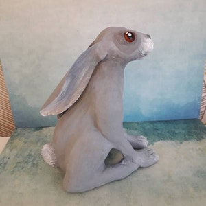 May include: A gray ceramic rabbit sculpture with red eyes and a white nose. The rabbit is sitting upright with its ears perked up.