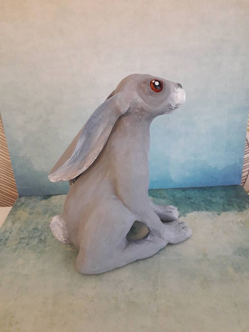 May include: A gray ceramic rabbit sculpture with red eyes and a white nose. The rabbit is sitting upright with its ears perked up.