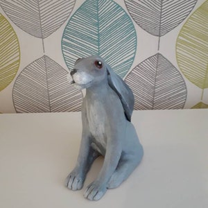 May include: A gray ceramic hare figurine with brown eyes. The hare is sitting with its ears perked up and its tail tucked behind its legs.