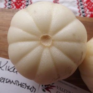 Peut inclure: Deux melons blancs à surface striée et un petit trou au centre. Les melons sont étiquetés "Kika Chrysanthemum".