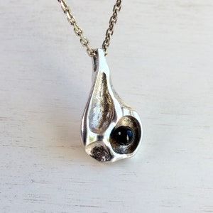 May include: A silver pendant necklace with a teardrop-shaped design. The pendant has a textured surface and a black gemstone in the center.