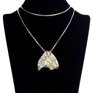 May include: A silver necklace with a textured, abstract pendant. The pendant is shaped like a leaf and has a rough, organic texture.