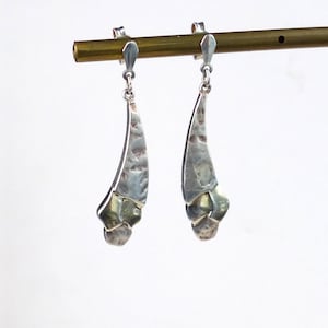 May include: A pair of silver earrings with a textured, geometric design. The earrings are hanging from a brass rod.
