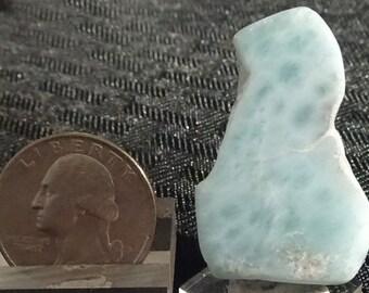 May include: A light blue, irregularly shaped, polished stone with white flecks. The stone is about the size of a U.S. quarter.