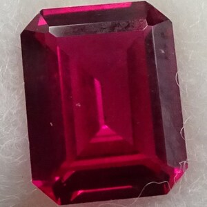 May include: A deep red emerald cut gemstone with a high polish.