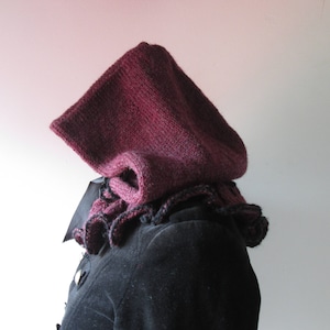 Könnte beinhalten: Eine burgunderfarbene gestrickte Kapuze mit einem schwarzen Häkelrand. Die Kapuze ist aus einem weichen, warmen Garn gefertigt und perfekt, um Sie im Winter warm zu halten.