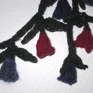 Könnte beinhalten: Eine gestrickte Girlande mit dunkelgrünen Blättern und roten und blauen blütenförmigen Ornamenten.