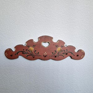 Può includere: Un portachiavi in legno con un ritaglio a forma di cuore e disegni floreali dipinti in rosso, giallo e nero.