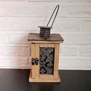 May include: A wooden candle lantern with a metal top and a decorative metal insert. The lantern has a handle and a latch.