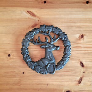 May include: A black cast iron trivet in the shape of a deer with antlers standing in a wreath of leaves.
