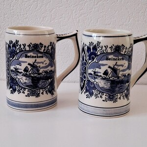 May include: Two blue and white ceramic beer mugs with a Dutch windmill scene and the word "Heineken" on each.