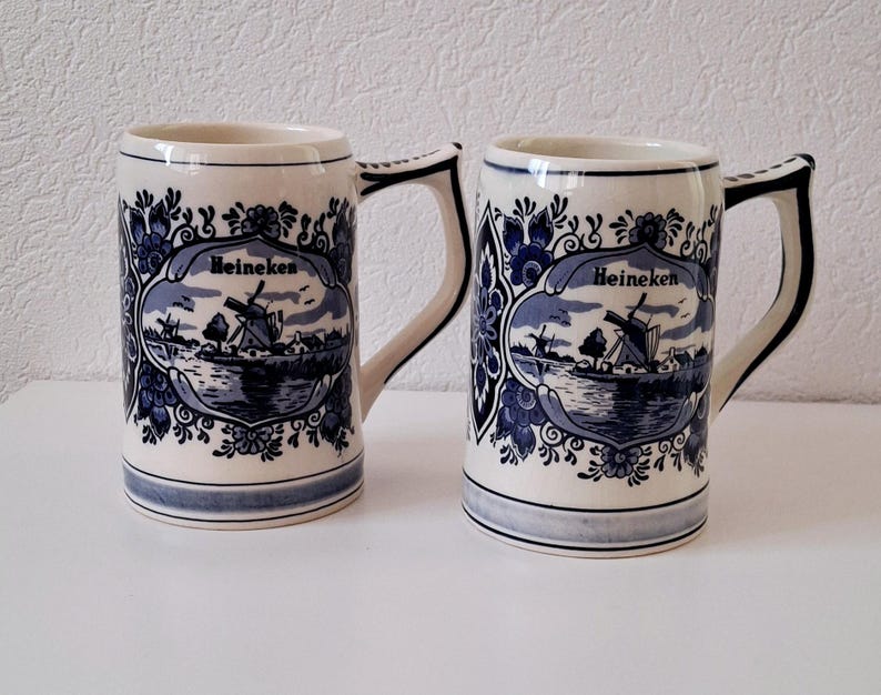 May include: Two blue and white ceramic beer mugs with a Dutch windmill scene and the word "Heineken" on each.