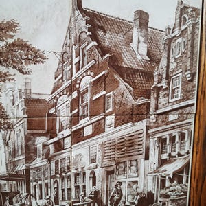 May include: A sepia-toned tile set depicting a European town scene. The artwork shows buildings, people, and a horse-drawn carriage. The tiles are framed in a dark wood.