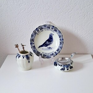 Può includere: Un filtro per tè in maiolica di Delft blu e bianco con un filtro a rete argentato, un vaso in maiolica di Delft blu e bianco con due cucchiai d'argento e un piatto in maiolica di Delft blu e bianco con un uccello blu e il testo "2 TIJ '86 J DOFFERS P.V. NIEUWEDIEP"