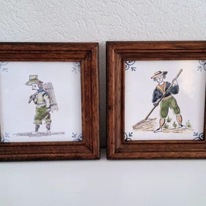 Può includere: Due piastrelle quadrate incorniciate con illustrazioni dipinte a mano di persone in abiti tradizionali. La piastrella a sinistra mostra una persona che porta un fascio di bastoni sulla schiena. La piastrella a destra mostra una persona che tiene un rastrello.