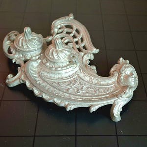 May include: Silver ornate inkwell with three inkwells and a cherub design.
