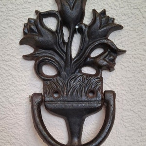 May include: Black cast iron door knocker shaped like a bouquet of tulips. The knocker has a ring handle and a pointed base.