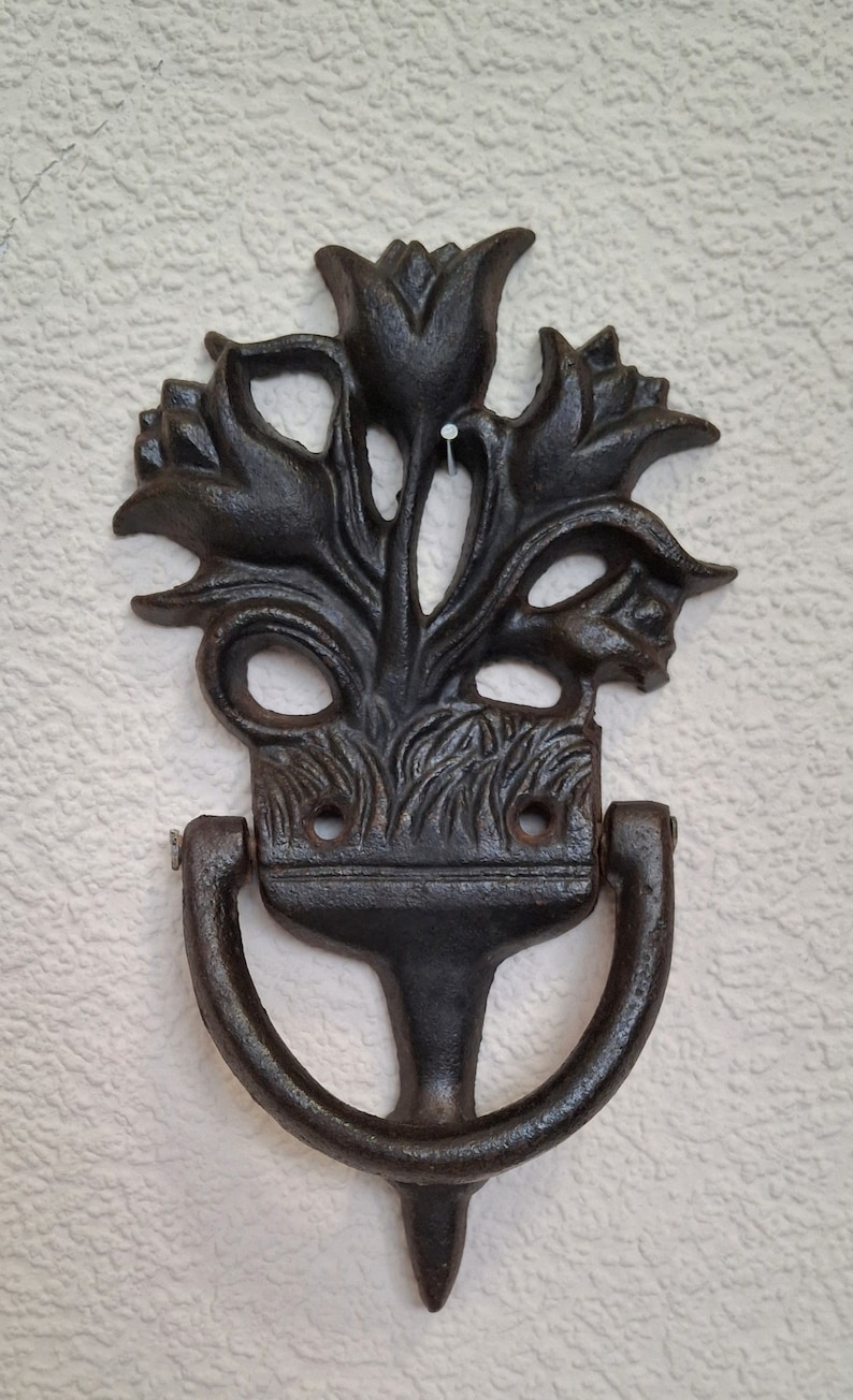 May include: Black cast iron door knocker shaped like a bouquet of tulips. The knocker has a ring handle and a pointed base.
