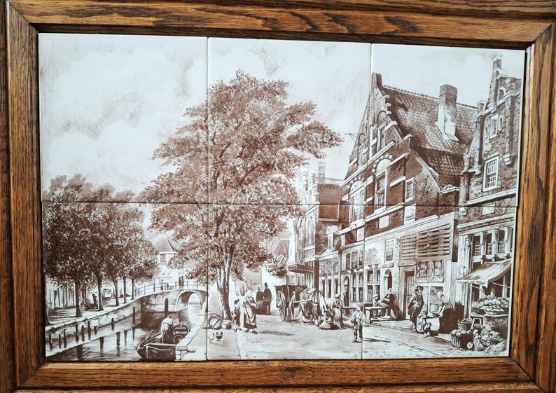 May include: A sepia-toned tile mural depicting a European town scene with a canal, bridge, and buildings. The artwork is framed in a dark wood. The scene includes people, trees, and boats, creating a vintage aesthetic.