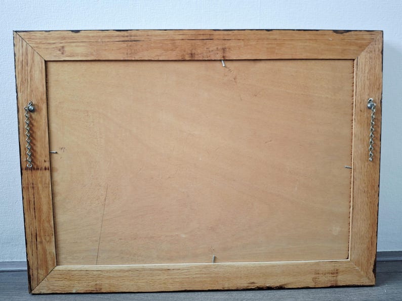 May include: Back of a rectangular wooden picture frame. The frame is made of light brown wood with a darker brown border. Metal chain and hardware are attached for hanging. The back is a light brown wood panel.