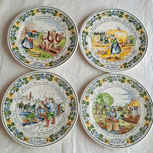May include: Set of four decorative ceramic plates depicting scenes of the four seasons. Each plate features a colorful illustration of a different season, with text in Dutch describing the season and its activities. The plates are white with blue, yellow, green, and red accents.