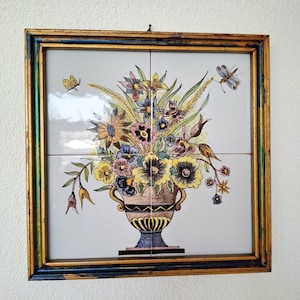 Könnte beinhalten: Gerahmte Blumenfliesenkunst. Das Kunstwerk zeigt einen bunten Blumenstrauß in einer dekorativen Vase mit Schmetterlingen. Der Rahmen ist gold und blau. Das Kunstwerk besteht aus vier Fliesen.