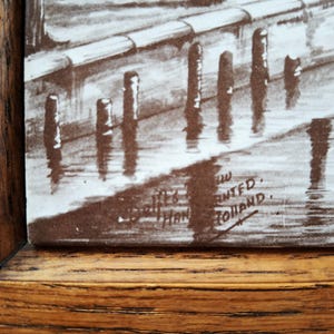 May include: A sepia-toned print of a waterside scene, framed in a wooden frame. The artwork depicts a row of posts in the water, with reflections. The print is signed and includes the text "Printed in Holland."