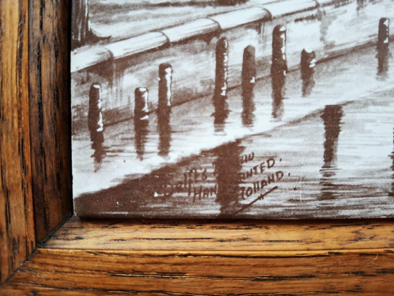 May include: A sepia-toned print of a waterside scene, framed in a wooden frame. The artwork depicts a row of posts in the water, with reflections. The print is signed and includes the text "Printed in Holland."
