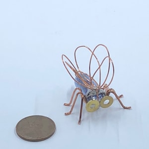 May include: A small, copper wire sculpture of a fly with blue wings and gold accents. The fly is about the size of a penny.