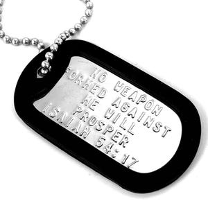 May include: A silver military dog tag with a black rubber coating. The tag has the text "NO WEAPON FORMED AGAINST HE WILL PROSPER ISAIAH 54:17" engraved on it.