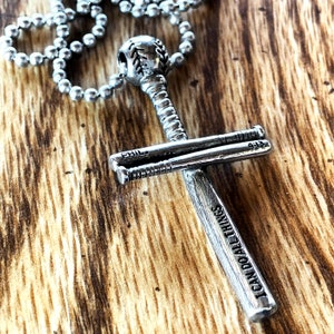 May include: Silver baseball bat cross necklace with a baseball charm and the words "I can do all things" engraved on the bat. The cross is made of two baseball bats.