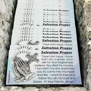 May include: A stack of white cards with the text "Salvation Prayer" printed on them. The top card has a drawing of praying hands and a cross. The text on the top card reads "Dear Lord Jesus, I know that I am a sinner, and I ask for Your forgiveness. I believe You died for my sins. I turn from my sins and invite you to come into my heart and life. I want to trust and follow You as my Lord and Savior. In Your Name, amen."