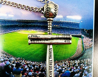 May include: Silver baseball bat cross necklace with the words "Phil. 4:13" and "I can do all things" engraved on the bats. The necklace is displayed against a backdrop of a baseball stadium.