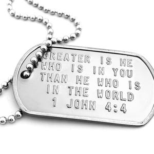 Può includere: Un collare con un ciondolo a forma di medaglia militare in argento con inciso un versetto biblico: "GREATER IS HE WHO IS IN YOU THAN HE WHO IS IN THE WORLD 1 JOHN 4:4".