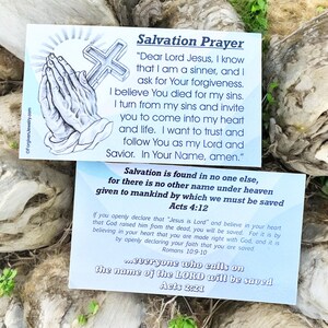 May include: Two blue and white cards with a Christian prayer for salvation. The first card features a drawing of hands in prayer with a cross. The text on the card reads "Salvation Prayer" and includes a prayer to Jesus. The second card features the text "Salvation is found in no one else, for there is no other name under heaven given to mankind by which we must be saved Acts 4:12". The card also includes a quote from Romans 10:9-10 and Acts 2:21.