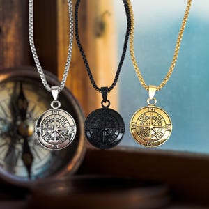 May include: Three compass necklaces with different colored chains. The necklaces have silver, black, and gold compass pendants.