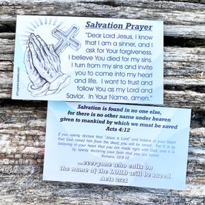 May include: Two blue and white cards with a Christian prayer for salvation. The top card features a drawing of hands in prayer with a cross. The text on the card reads "Salvation Prayer" and includes a prayer to Jesus. The bottom card features the text "Salvation is found in no one else..." and includes bible verses from Acts 4:12, Romans 10:9-10, and Acts 2:21.