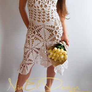 May include: A white crochet dress with a delicate floral pattern. The dress is sleeveless and has a loose fit. The model is wearing the dress with a bouquet of yellow flowers.