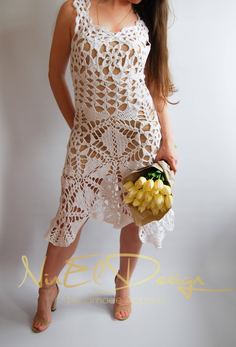 May include: A white crochet dress with a delicate floral pattern. The dress is sleeveless and has a loose fit. The model is wearing the dress with a bouquet of yellow flowers.