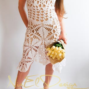May include: White crochet dress with a delicate floral pattern. The dress has a loose fit and a flowing skirt. The model is wearing the dress with a bouquet of yellow flowers.