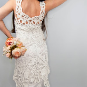 May include: A white crochet dress with a low back and a flowing skirt. The dress is made with delicate lace and has a bohemian style.