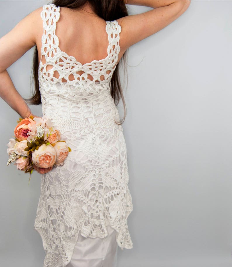 May include: A white crochet dress with a low back and a flowing skirt. The dress is made with delicate lace and has a bohemian style.