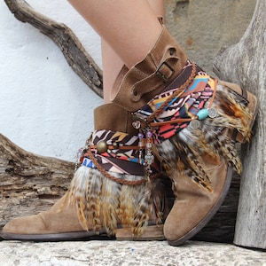 May include: Brown suede ankle boots with colourful fabric and feather trim. The boots have a buckle closure and are decorated with beads and charms.